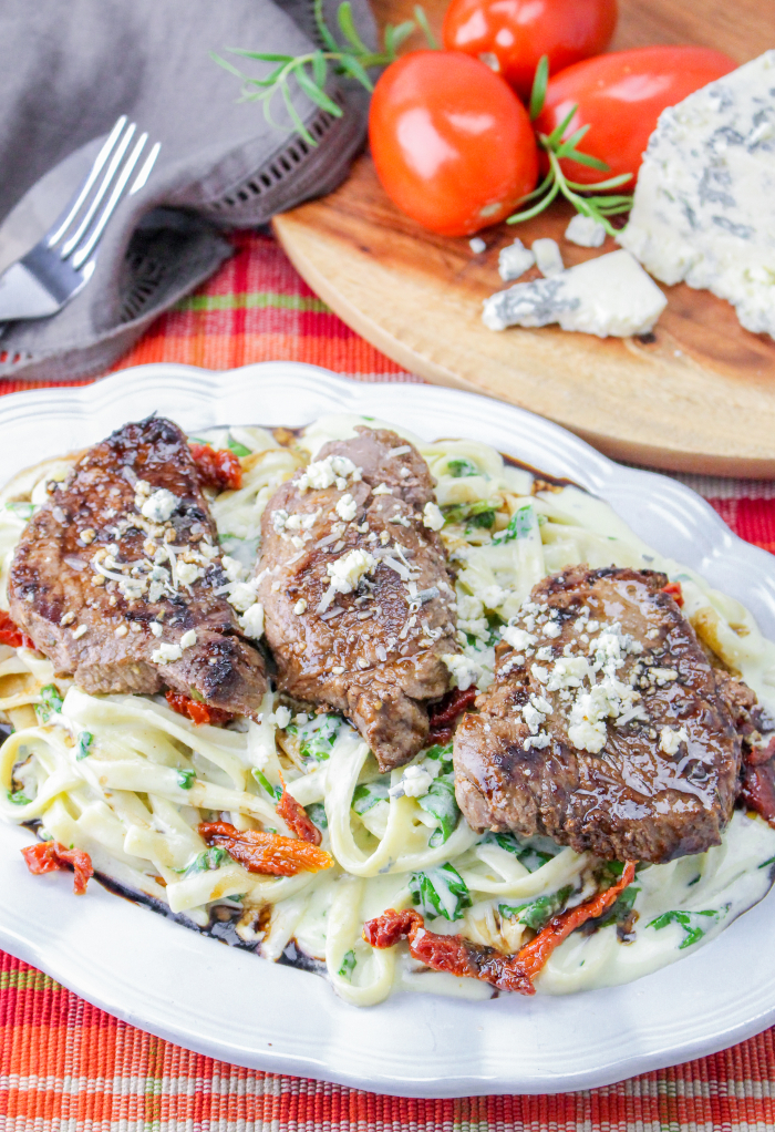 Top view of a white platter with fettuccini Alfredo topped with steak.