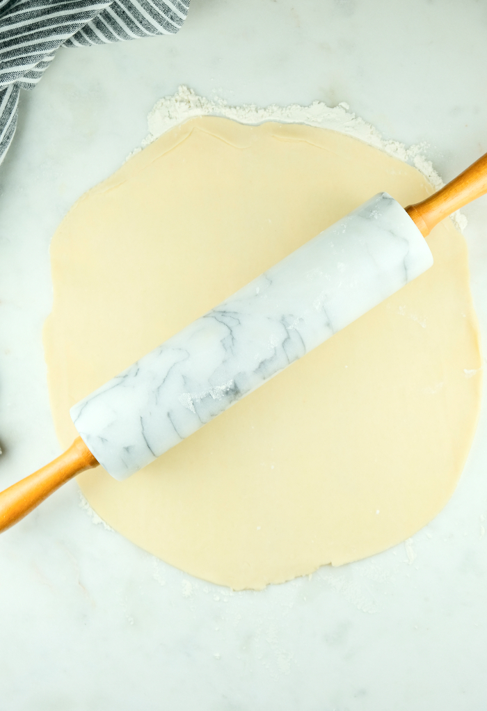 Cookie Dough with a rolling pin flattening it.