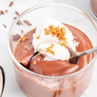 Chocolate pudding made from scratch in a clear dessert dish topped with whipped cream and a sprinkle of brown sugar.