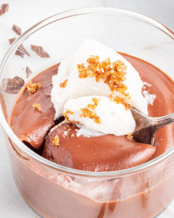 Chocolate pudding made from scratch in a clear dessert dish topped with whipped cream and a sprinkle of brown sugar.