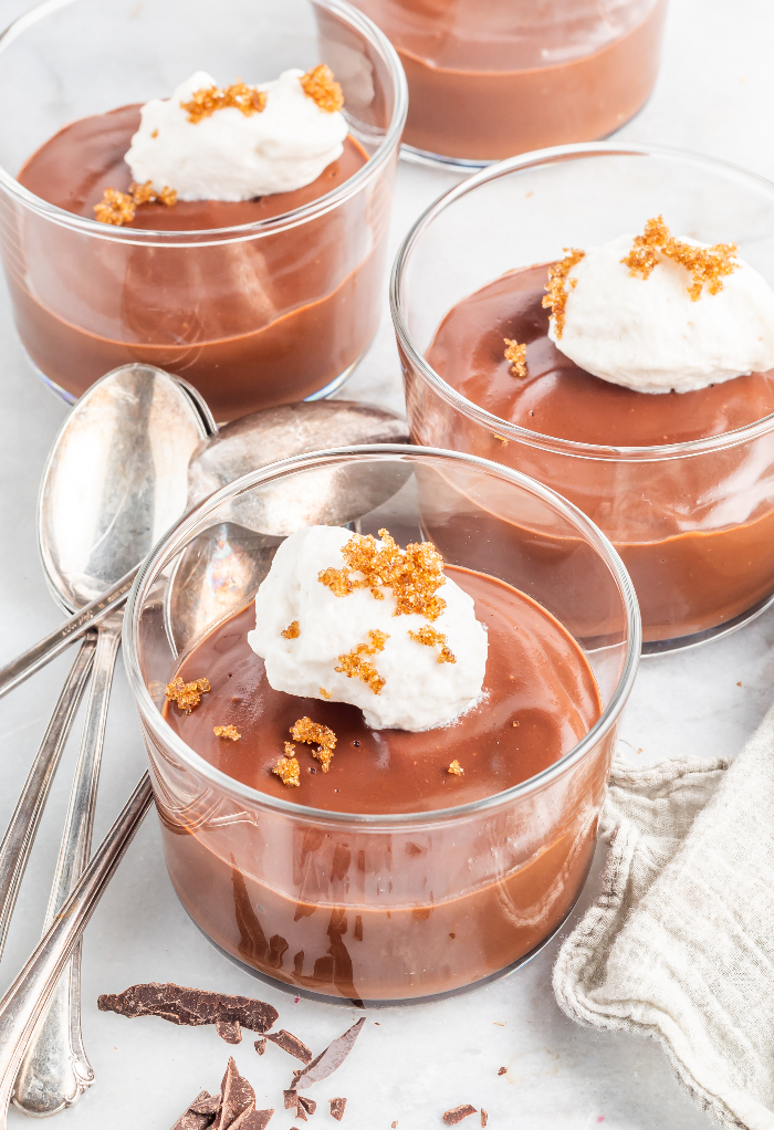 Multiple dessert dishes of chocolate pudding topped with whipped cream.
