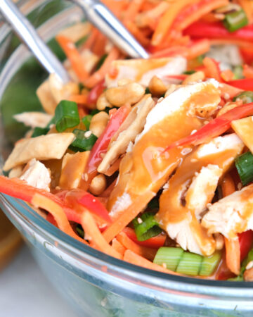 Healthy Chinese chicken salad with fresh veggies and a peanut dressing in a clear salad bowl.