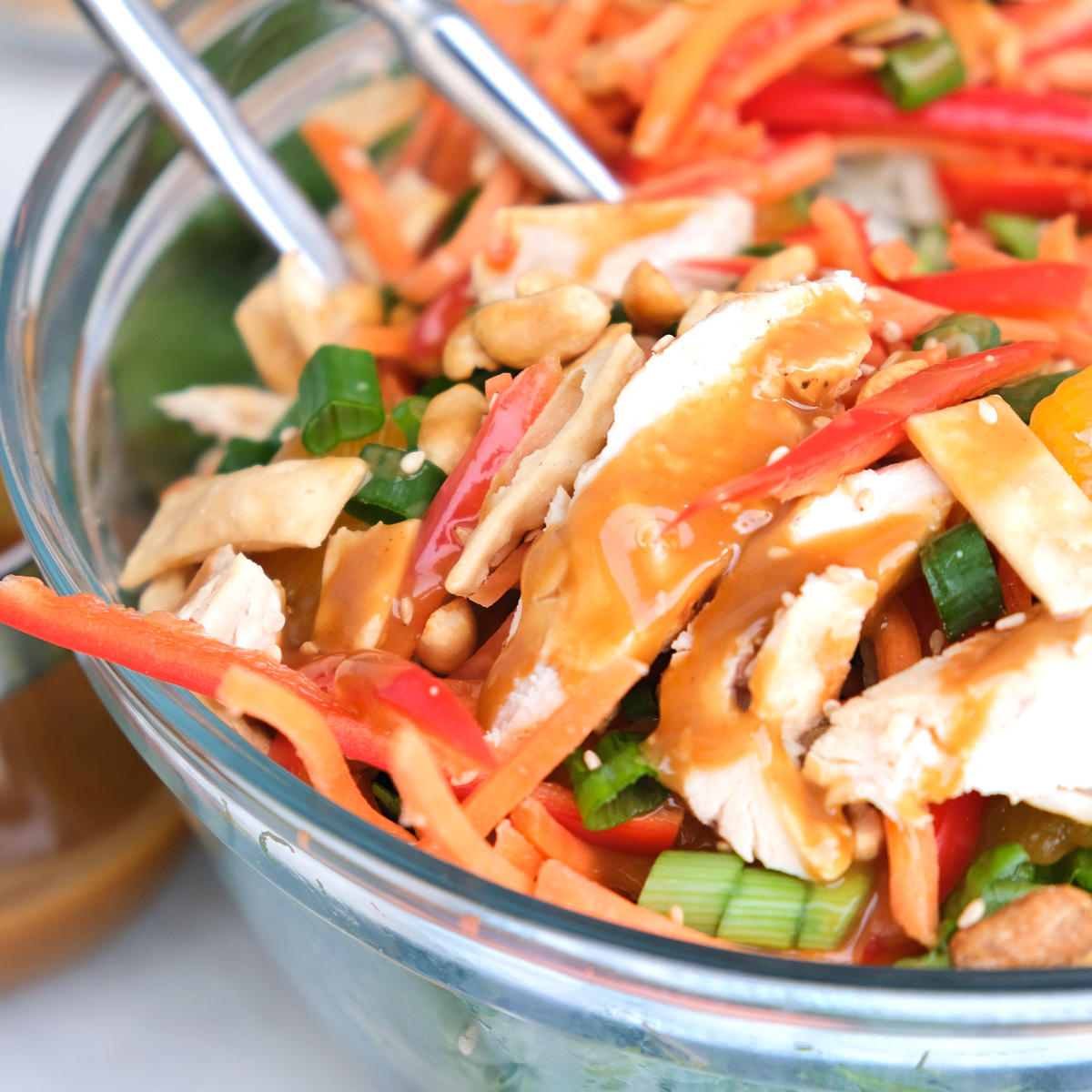 Healthy Chinese chicken salad with fresh veggies and a peanut dressing in a clear salad bowl.