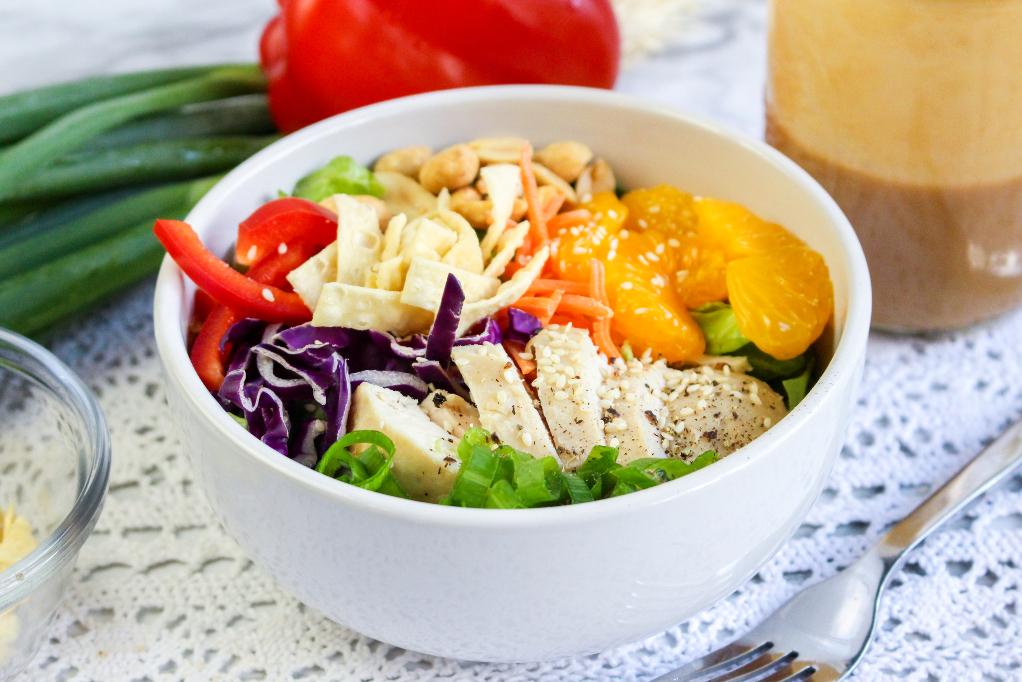 Chinese chicken salad in a white bowl with peanut salad dressing on the side. 