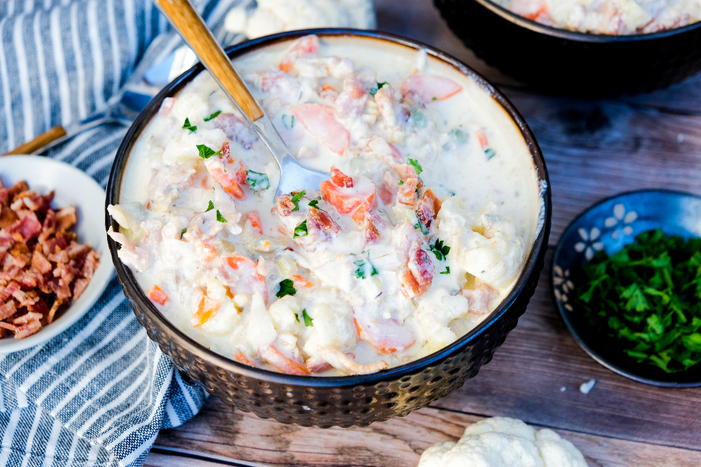 Low carb clam chowder soup in a brown bowl with bacon on the side. 