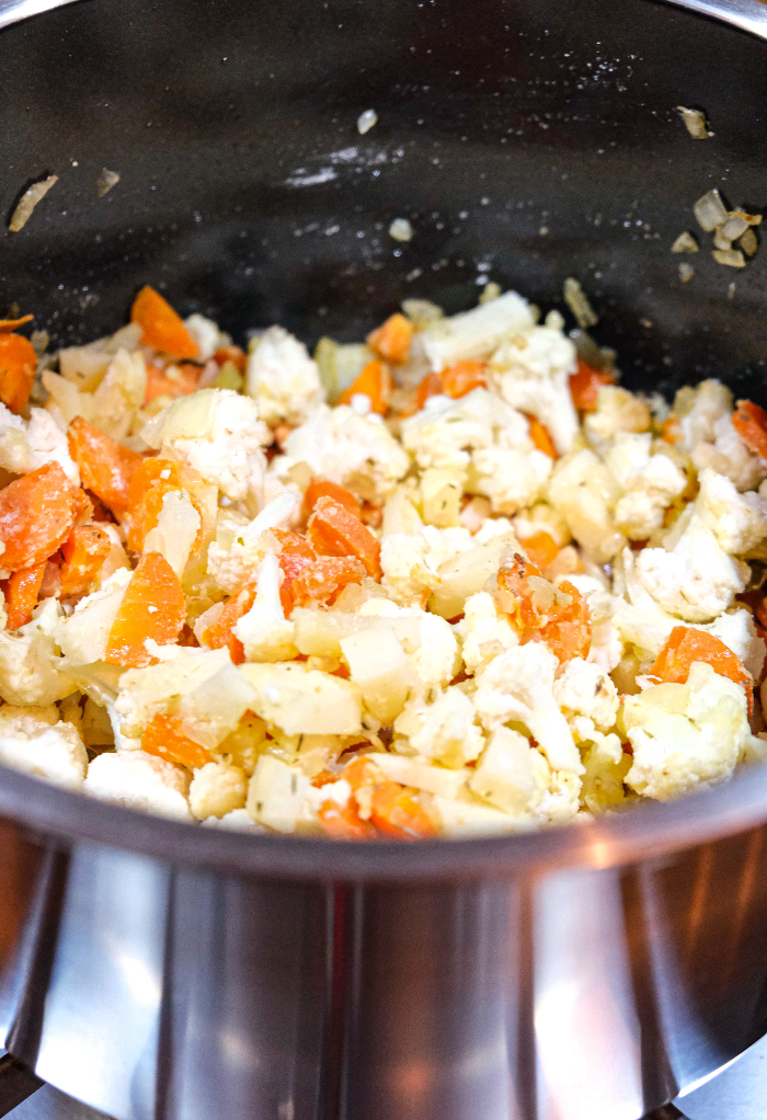 Cauliflower florets with carrots in a stockpan.