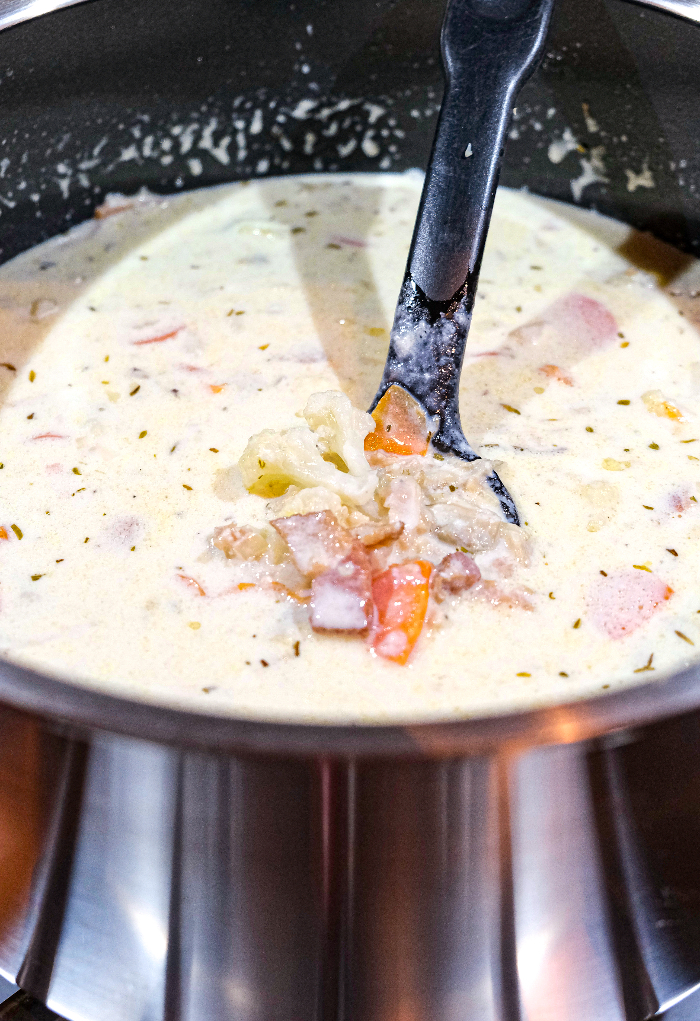 Clam juice and half and half added to clam chowder simmering in a stockpot. 