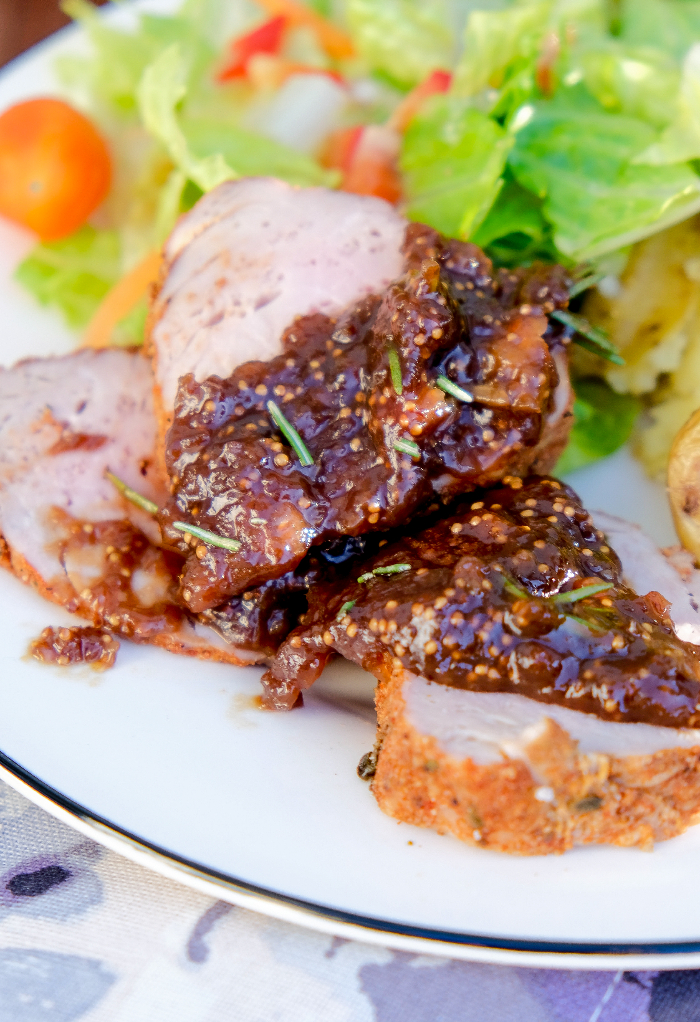 Sliced pork tenderloin topped with a dijon fig sauce on a white dinner plate. 