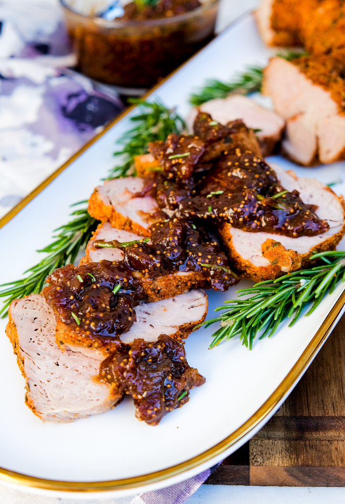 Pork tenderloin sliced on a white serving dish topped with fig sauce. 