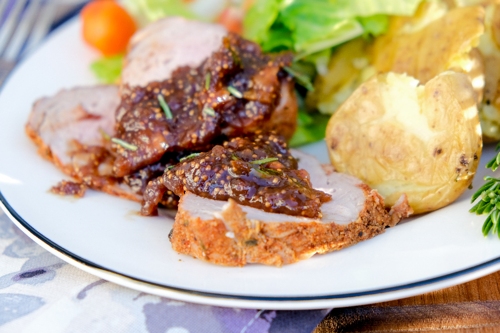 A white dinner plate with sliced pork tenderloin with fig sauce. 