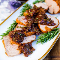 Sliced pork topped with a fig sauce on a white platter.