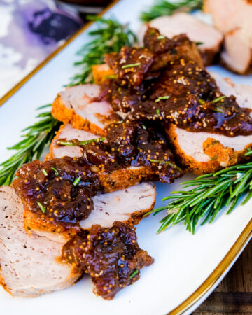 Sliced pork topped with a fig sauce on a white platter.