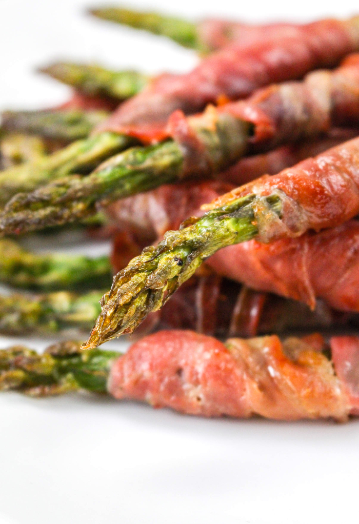 Fresh asparagus wrapped prosciutto on a white serving plate. 