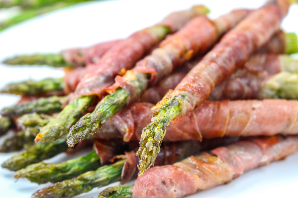 Fresh asparagus wrapped in prosciutto on a white plate. 