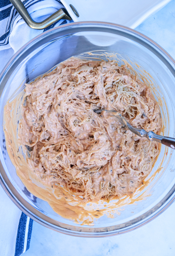 SauerKraut mixed with thousand island dressing and mayonnaise in a clear mixing bowl. 