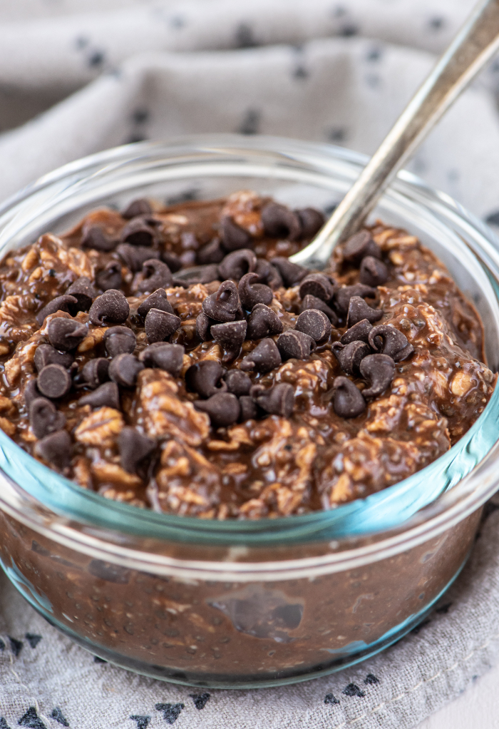 Chocolate overnight oats in a clear jar with a spoon ready to eat. 