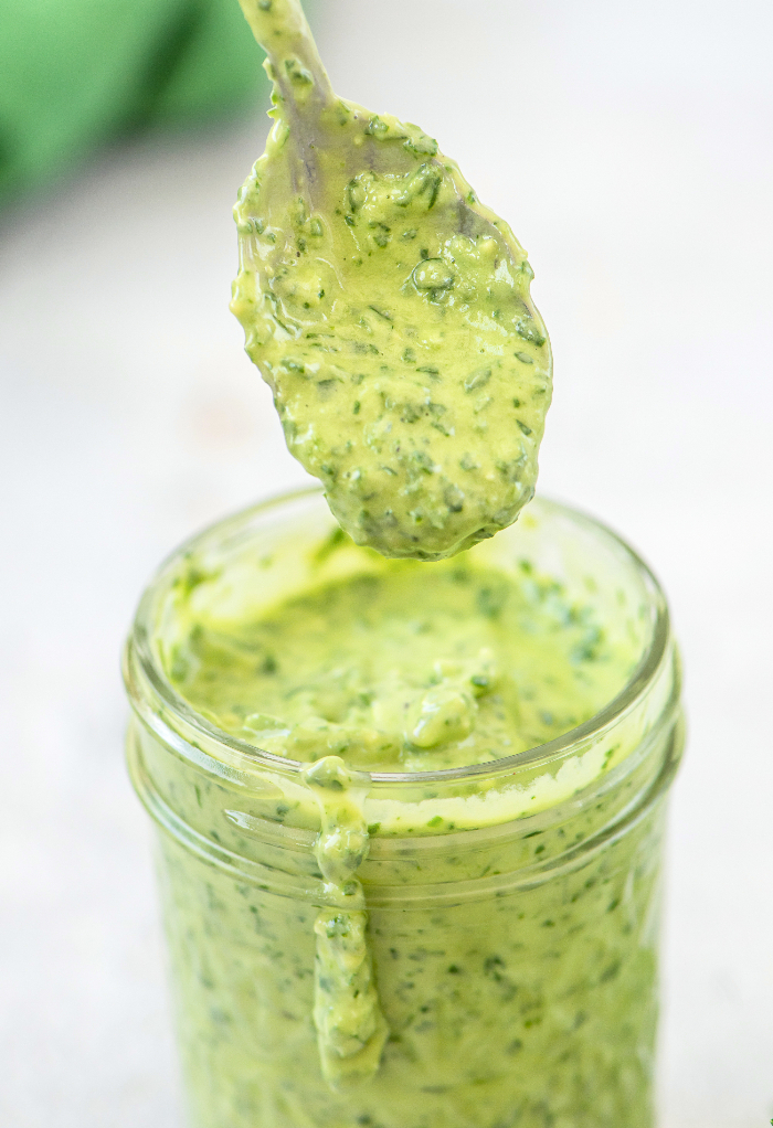 Homemade green goddess dressing in a mason jar with a spoon dipped in the jar. 