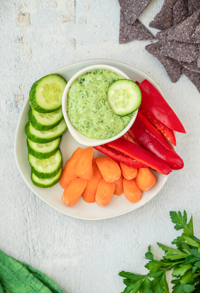 Green goddess dip in a white bowl surrounded by vegetables on a white plate. 