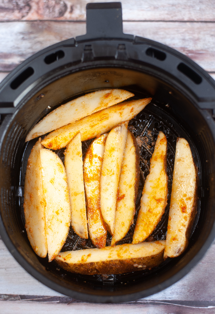 Sliced potato wedges in an air fryer basket ready to cook.