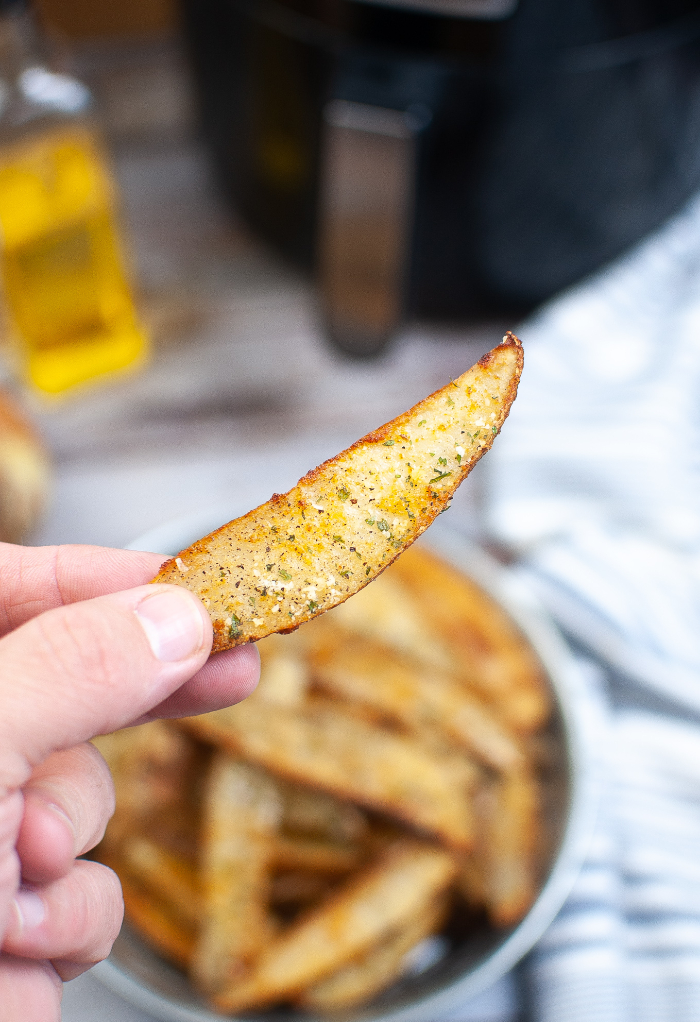 Cooked potato wedge picked up with fingers ready to eat. 