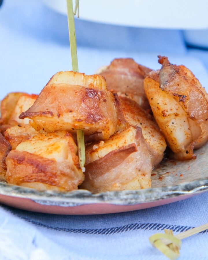 Scallops wrapped in bacon cooked in an air fryer on a tan plate.
