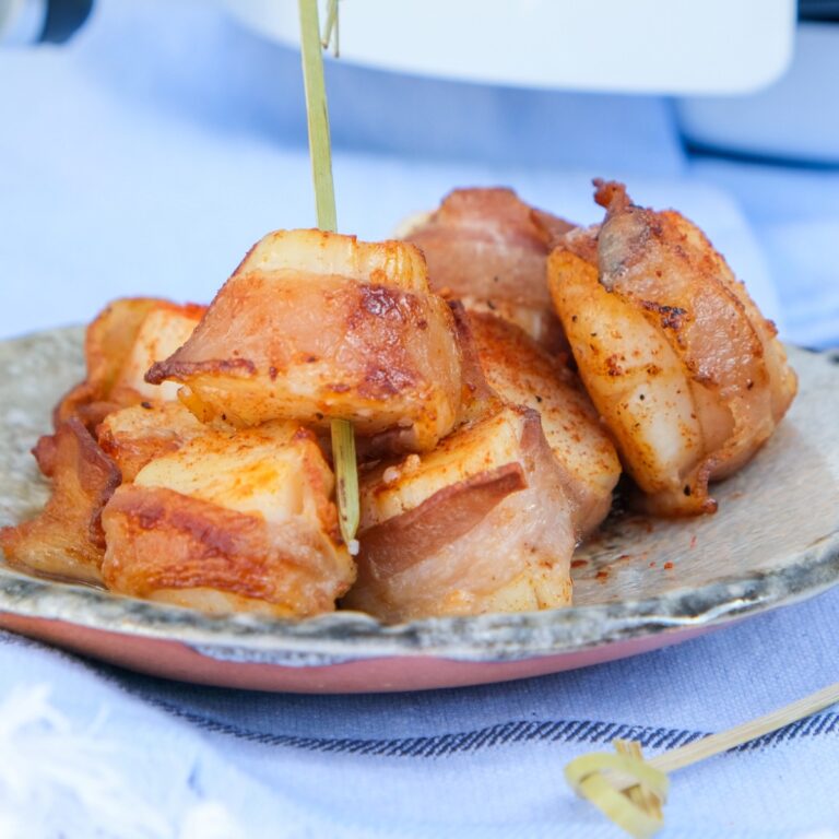 Scallops wrapped in bacon cooked in an air fryer on a tan plate.