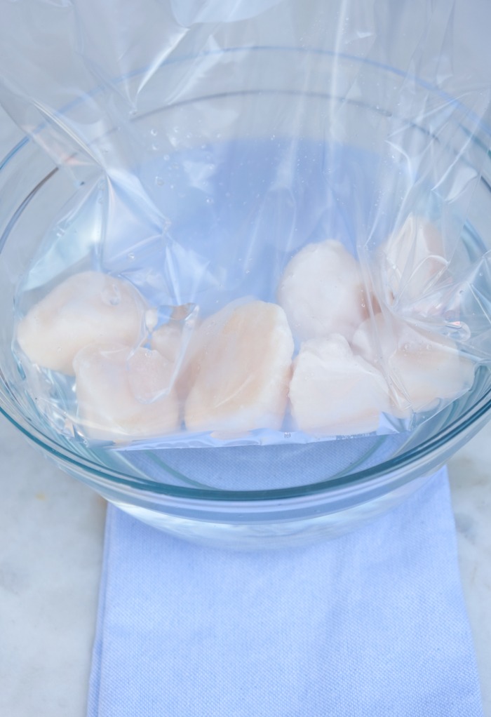 Plastic bag of frozen scallops in a bowl of cool water defrosting. 