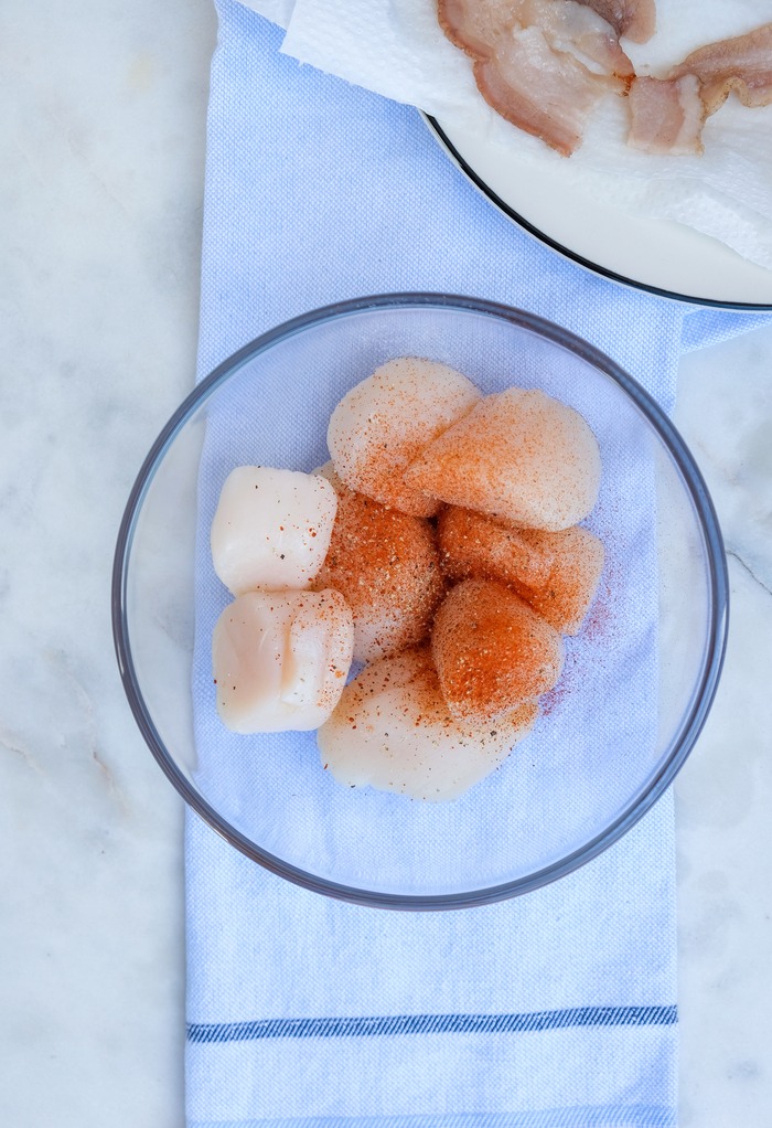 Scallops in a clear mixing bowl seasoned with salt, pepper and paprika. 