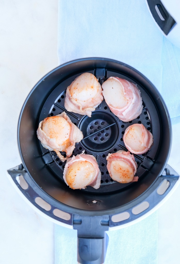 Scallops wrapped in a slice of bacon placed in an air fryer ready to cook. 