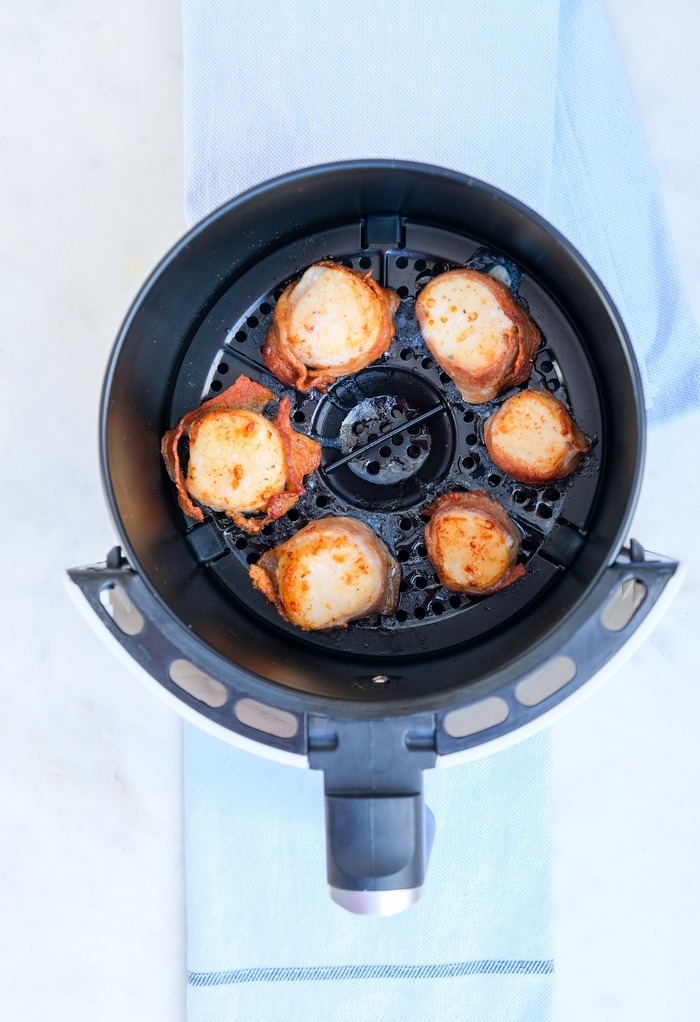 Cooked scallops wrapped in bacon sitting in an air fryer..