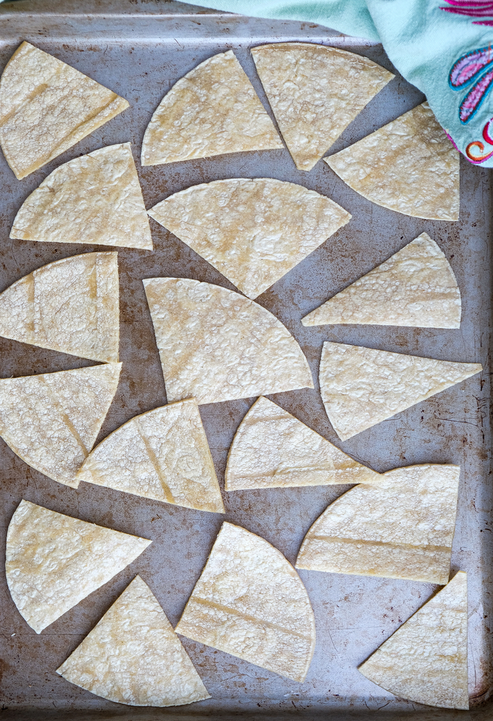 Corn tortillas cut into triangles placed on a baking sheet to bake.