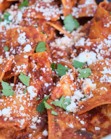 Close view of chilaquiles in a skillet topped with cheese and cilantro.