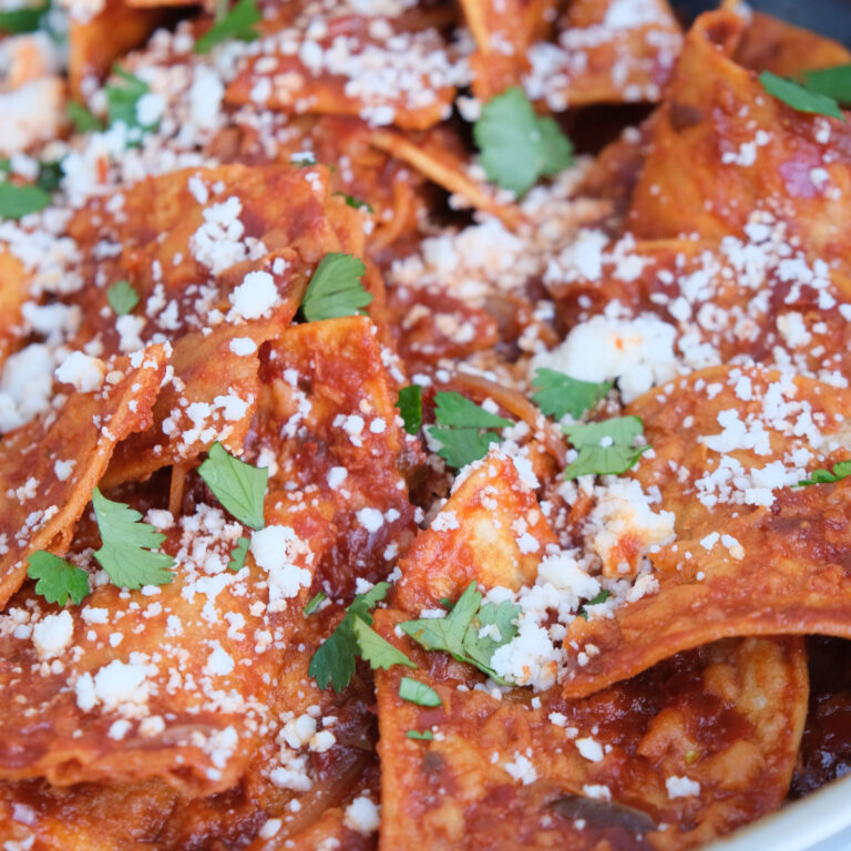 Close view of chilaquiles in a skillet topped with cheese and cilantro.
