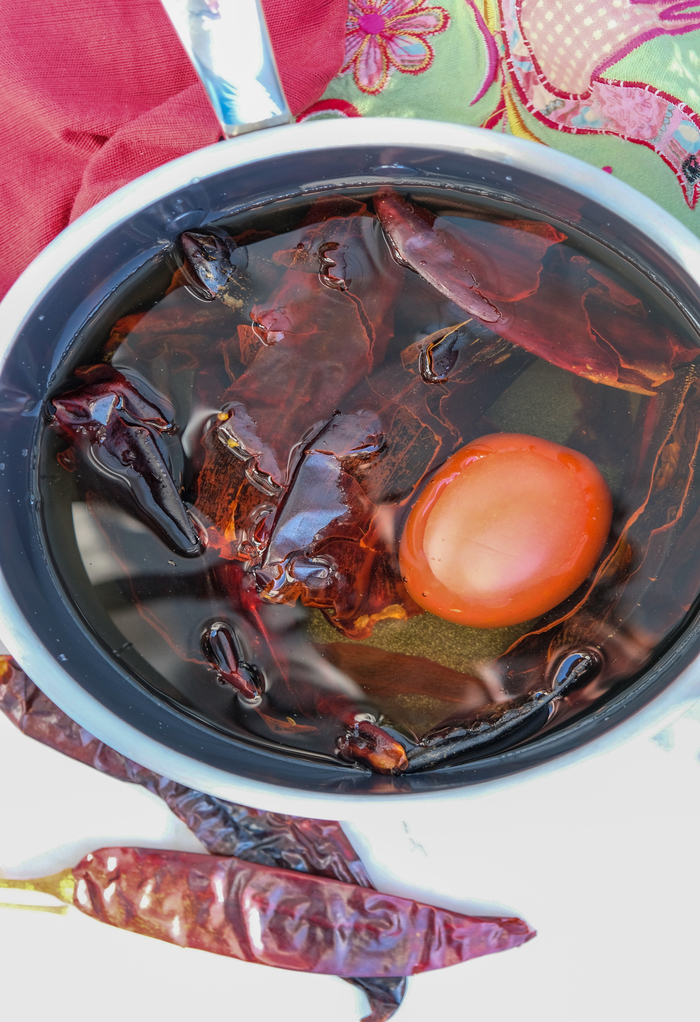 Saucepan with chile pods and a roma tomato simmering. 