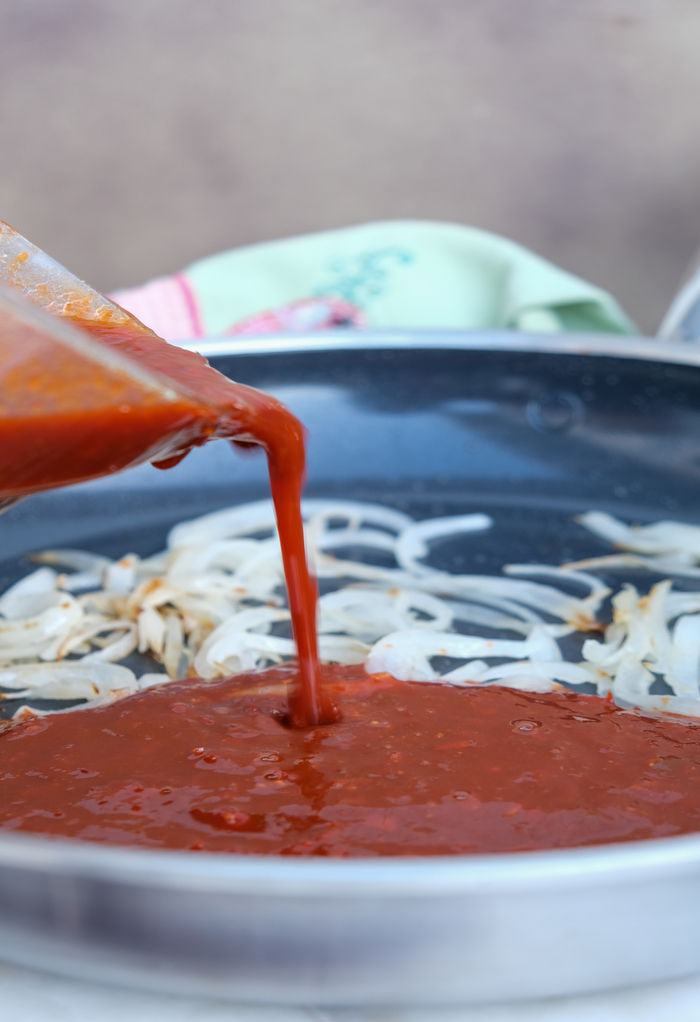 Sauteed onion in a skillet with chile sauce.