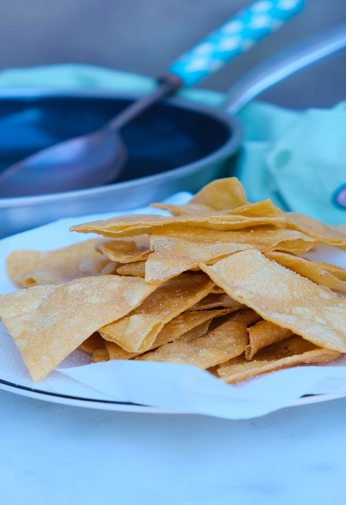 Fried tortillas draining on a paper towel over a plate. 