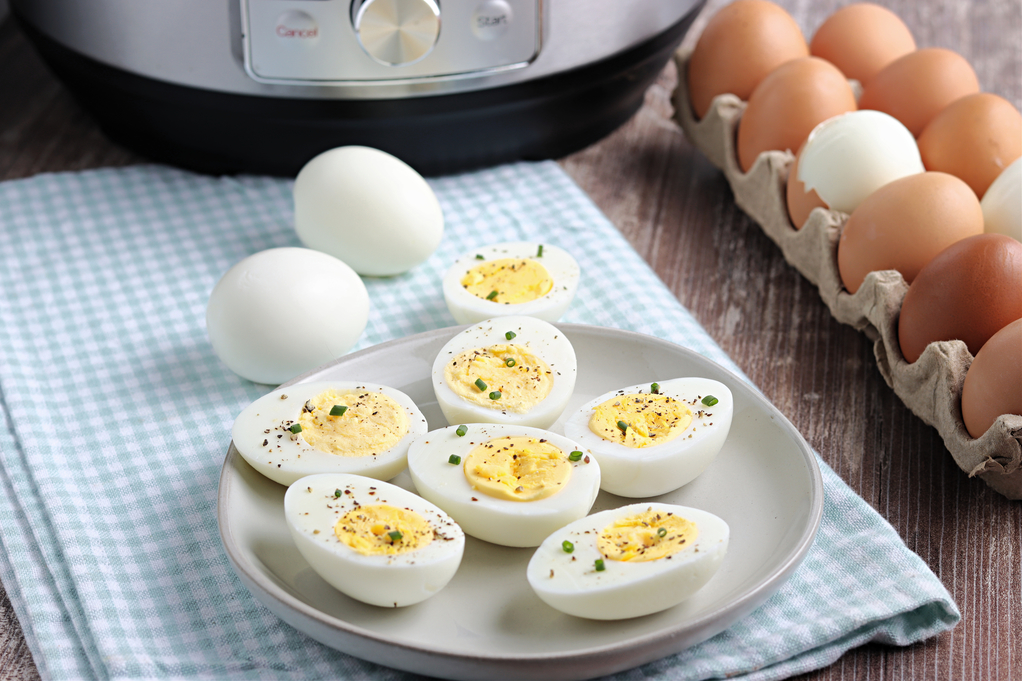 Fresh eggs on the side of a dish with hard boiled eggs on a serving dish. 