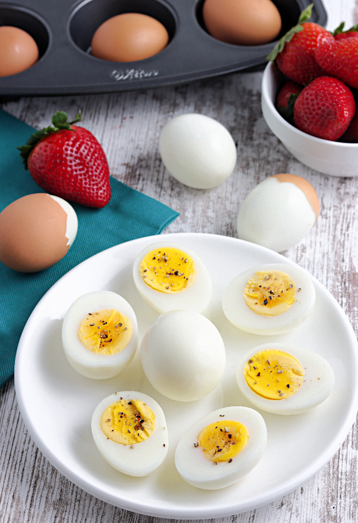 Top view of hard boiled eggs on a white plate with strawberries on the side. 