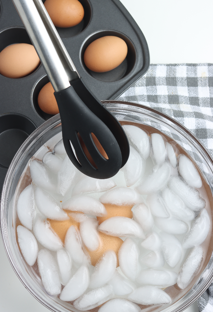 Cooked eggs placed in a clear bowl of ice water. 