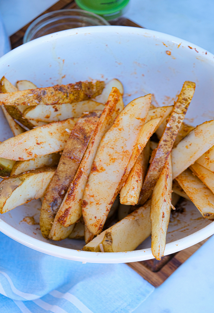 Sliced potato wedges in a white bowl seasoned with spices.