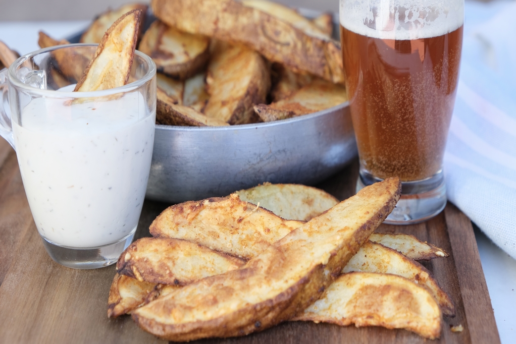 Close view of potato wedges in a bowl with a beer on the side.