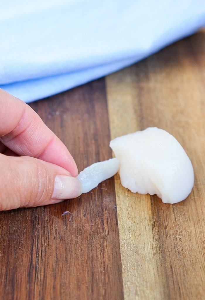 Gently peeling the soft muscle on the side of a scallop.