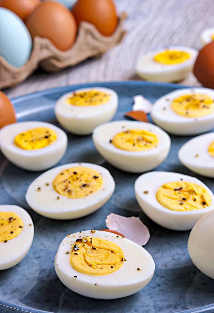 Hard boiled eggs sliced in half with salt and pepper on a blue plate. 