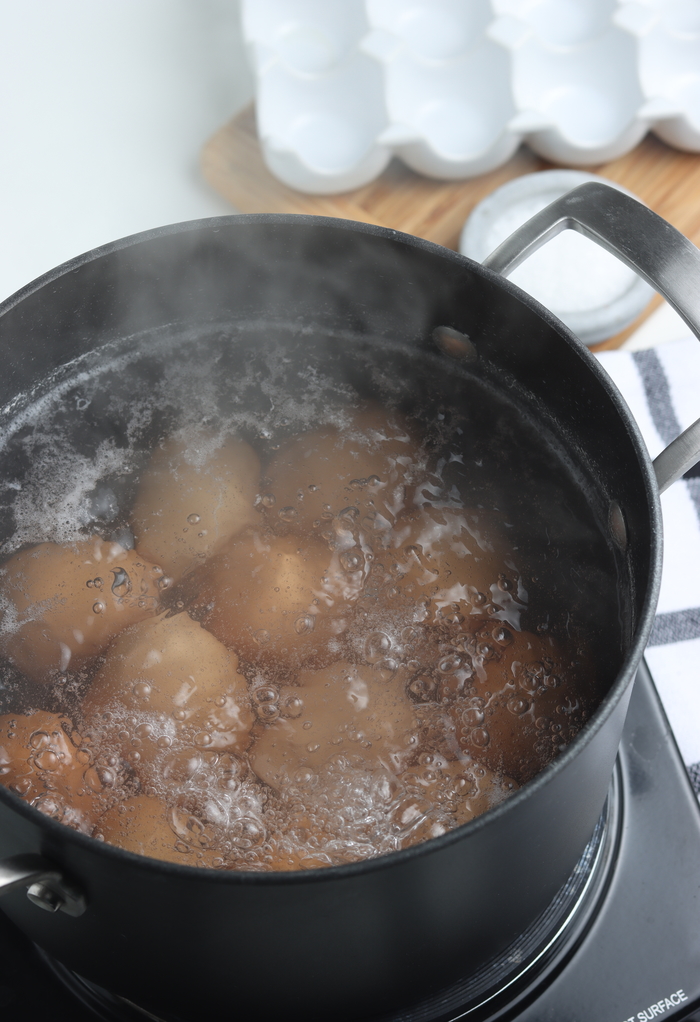 Boiling pot of water with eggs in them cooking them. 
