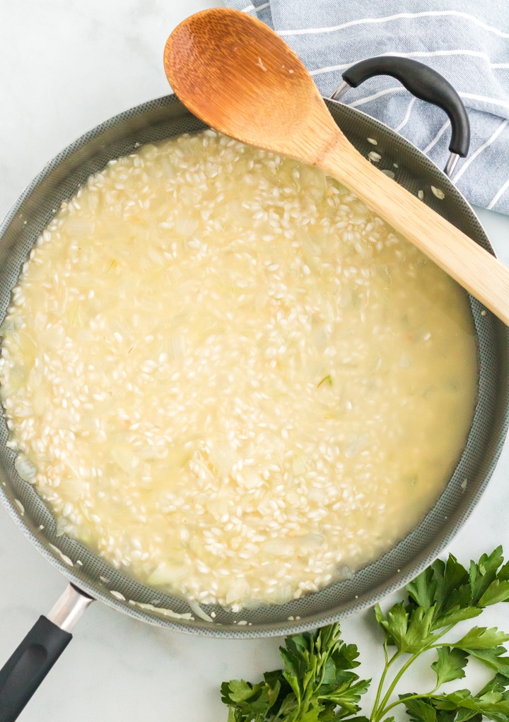 Adding broth to risotto in a large skillet. 