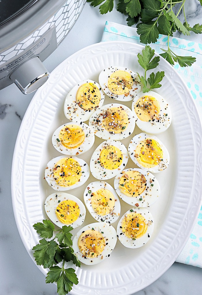 Top view of hard boiled eggs cooked in a crock pot on a white serving platter. 