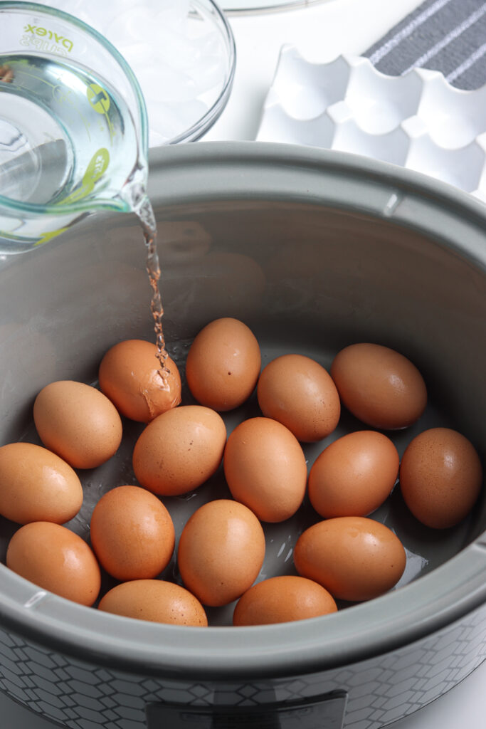 Pouring water over eggs in a Crock Pot to hard boil. 