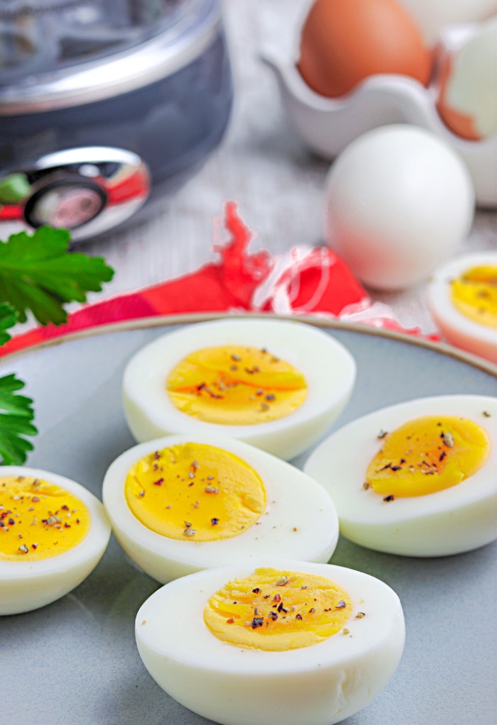 Sliced hard boiled eggs on a gray plate topped with salt and pepper. 