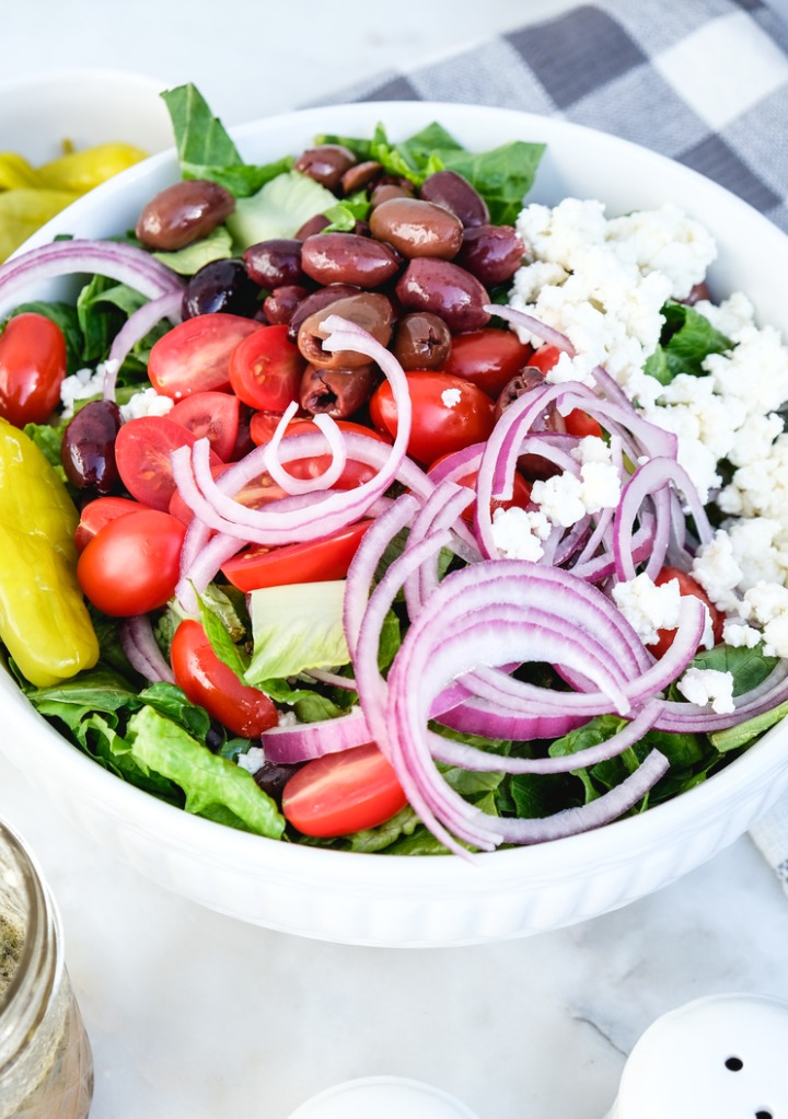 Salad prepared before tossing in a white serving bowl. 