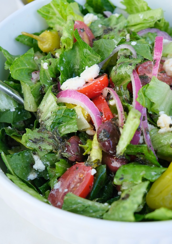 Homemade Greek salad with dressing in a white serving bowl. 